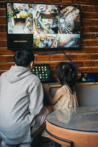 A homeowner reviews an alarm panel while a monitoring operator handles an alert on a computer.